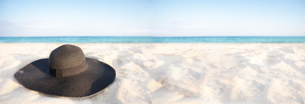 Banner Black hat on a background of the sea. Beach accessory on white sand. Straw panama on the background of the ocean