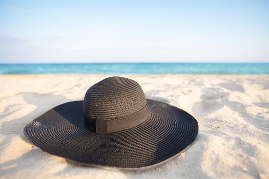 Black hat on a background of the sea. Beach accessory on white sand. Straw panama on the background of the ocean