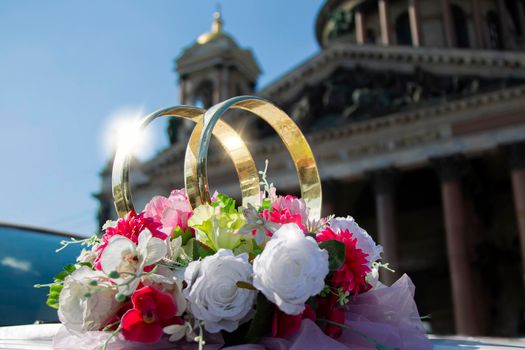 Wedding day. Wedding rings on a car with a bouquet on the background of a beautiful building. Betrothal.