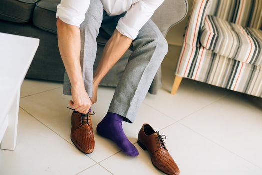The man in gray slacks and a purple dress socks brown shoes with laces sitting on the couch.