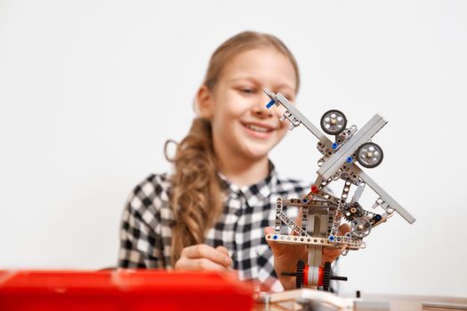 Selective focus of interesting robot in hands of young smiling girl sitting at table. Close up of vehicle made using building kit fo children. Concept of science engineering.