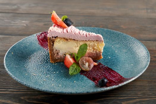 Close up of classic, traditional cheesecake served with blueberries and cranberries on blue plate with purple decoration on wooden table in restaurant. Concept of yummy sweet dessert, serving.