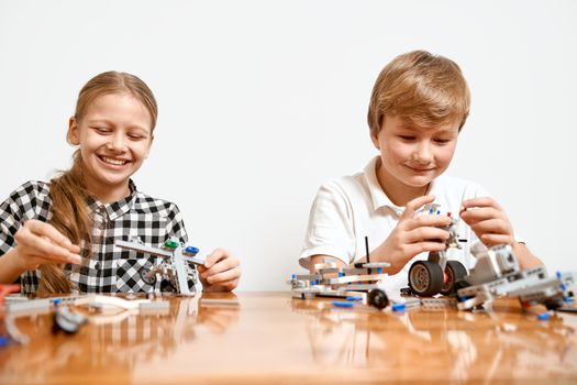 Interesting building kit for kids on table. Close up of boy and girl having fun at table, creating vehicles. Science engineering. Young friends laughing, chatting and working on project together.