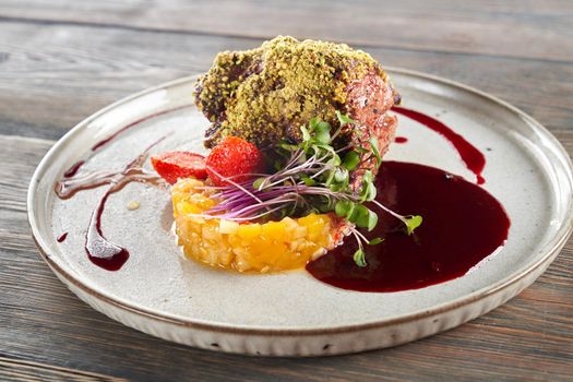 Tasty meal with fruits, berries and sprouts presented on ceramic white plate in luxurious restaurant. Close up view of beef meat with pistachio topping served with cranberry sauce on wooden table.