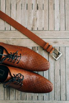 Brown man's shoes with laces on a wooden background and a brown belt.