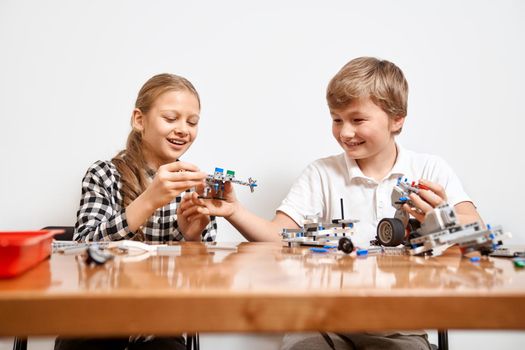 Interesting building kit for kids on table. Close up of boy and girl having fun at table, creating vehicles. Friends laughing, chatting and working on project together. Concept of science engineering.