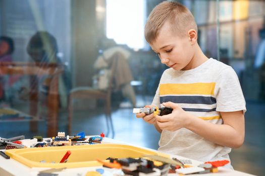 Front view of building kit for group of kids creating toys, having positive emotions and joy. Selective focus of lovely caucasian boy working on project, taking colorful parts.