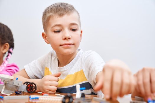 Front view of building kit for group of multiracial kids creating toys, having positive emotions and joy. Selective focus of lovely caucasian boy working on project, taking colorful parts.