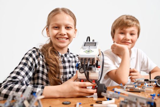 Front view of boy and girl creating robot using building kit for kids on table. Nice interested friends smiling, lookig at camera and working on project together. Concept of science engineering.