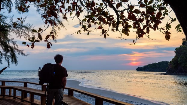 One man traveler with a backpack is standing looking at the sunset. beautiful nature landscape of colorful the sun on the sky at Koh Tarutao island, Satun, Thailand, 16:9 wide screen