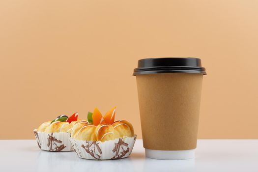 Coffee or tea in cardboard cup with pastry against beige background. Concept of hot drinks and take away food