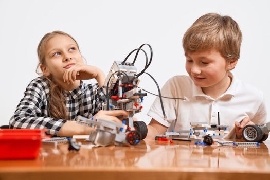 Building kit for kids on table. Front view of boy and girl having fun, creating vehicle. Science engineering. Nice interested friends working on project together, girl looking up and thinking.