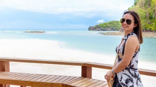 Landscape of the beach and the sea in summer sky and beautiful woman tourist wearing sunglasse, looking at the camera and smiling on Tarutao island, Satun, Thailand, 16:9