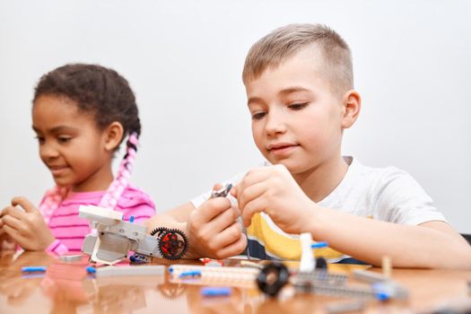 Front view of building kit for group of multiracial kids creating toys, having positive emotions and joy. Selective focus of lovely caucasian boy working on project, taking colorful parts.