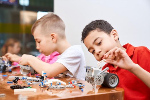 Side view of building kit with colorful pieces in box for group of multiracial kids creating robots, having positive emotions and joy. Close up of interested friends working on project.