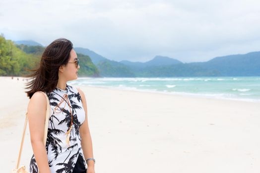 Beautiful woman tourist wearing sunglasse smiling looking at the nature landscape of the beach and the sea in summer sky on Tarutao island National Park, Satun, Thailand