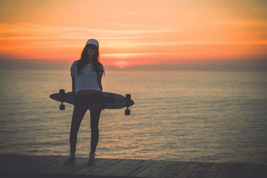 Beautiful and fashion young woman posing at teh sunset with a skateboard - File a little bit noisy