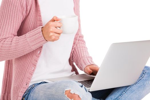 Young female student working with a laptop while drinking coffee, isolated over white background