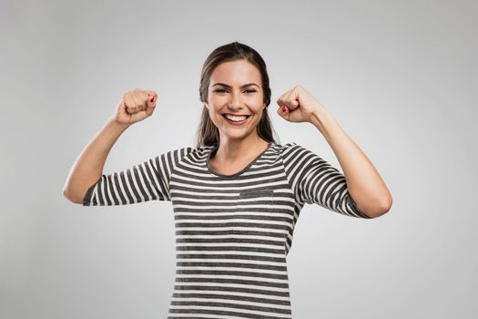Beautiful happy woman with arms up over a gray background