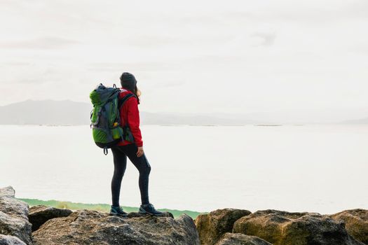 Woman with backoack enjoying the morning view of the coast