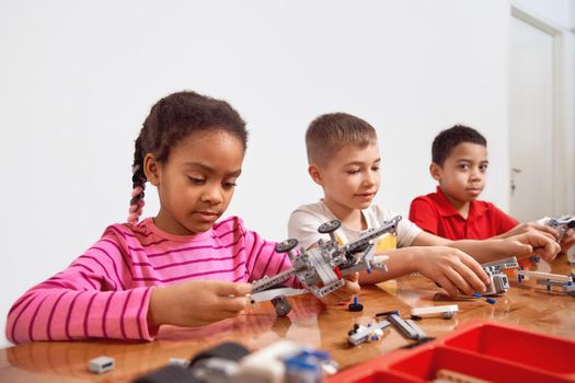 Side view of building kit with colorful peices in box for group of three multiracial kids creating toys, having positive emotions and joy. Close up of interested friends working on project.