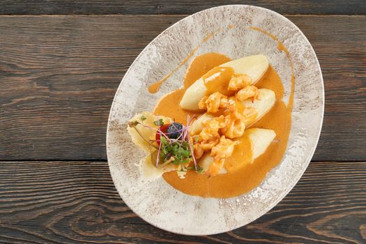 Delicious seafood with orange sauce on plate on table, three potato cutlets served with vegetables and sprouts. From above view of shrimps cooked in restaurant for dinner. Concept of food and cuisine.