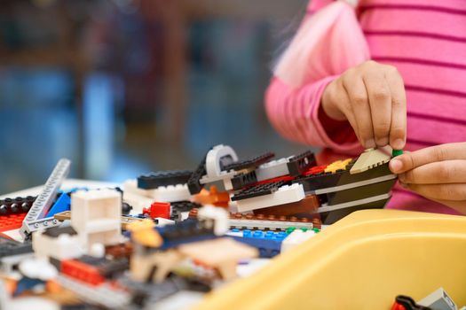 Front view of building kit for kids creating toys, having positive emotions and joy. Crop of incognito african girl working on project, hands taking colorful parts. Concept of science engineering.