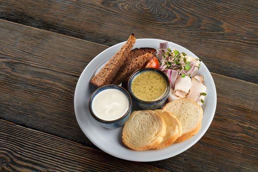 Top view of white and dark bread slices serves with sprouts, vegetables and pork fat on plate. Tasty snack with sour cream and green sauce in restaurant. Concept of traditional ukrainian cuisine.