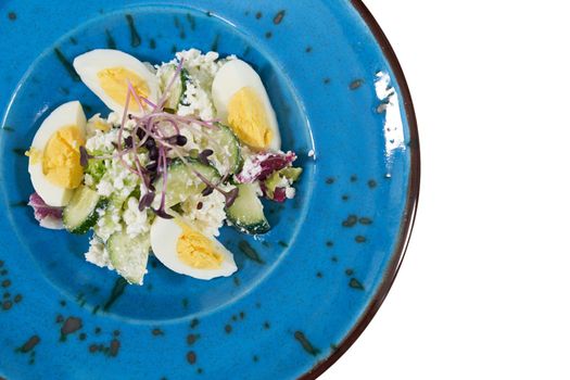 Top view close up of delicious salad with eggs,cucumber and greens in modern blue plate on white background. Concept of delicious and healthy food to maintain figure at home. 