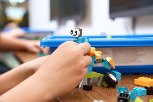 Selective focus of hands using building kit for kids, creating toys. Crop of incognito caucasian child working on project, taking colorful parts. Concept of science engineering.