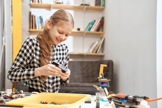 Selective focus of lovely smiling caucasian girl working on project, using colorful parts and having positive emotions and joy. Building kit for toys creating. Concept of science engineering.