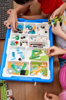 From above view of hands of incognito children taking details out of box and working on project. Colorful pieces from building kit for group of kids on table. Concept ofs cience engineering.