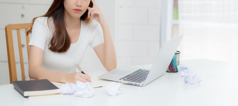 Young asian woman working with laptop computer think idea project and paper crumpled having problem on table at home, girl using notebook with frustrated and trouble, business and freelance concept.