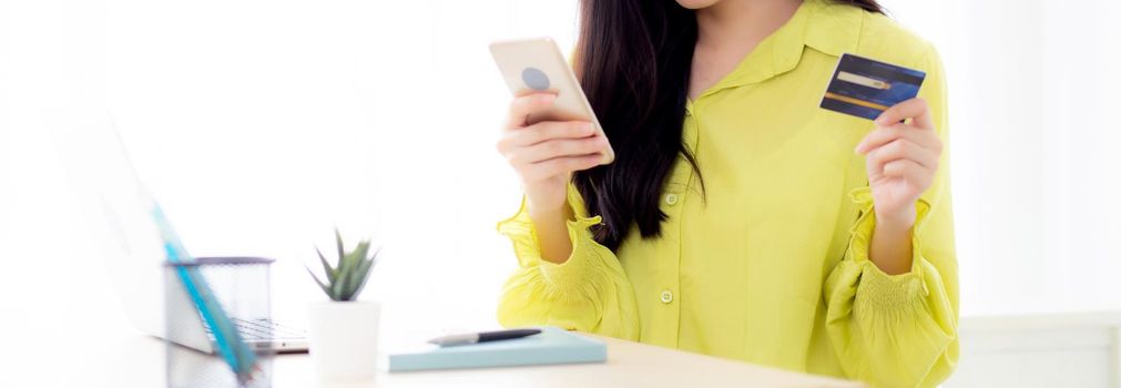 Young asian business woman using smart phone and holding credit card while online shopping and payment online with laptop computer on desk at home, female holding debit card, communication concept.