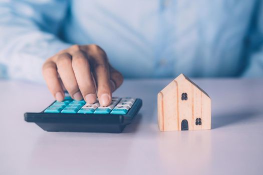 Hand of businessman planning and calculate expense and mortgage with calculator and home on desk, insurance and budget of residential, examining of loan and residence, business and property concept.