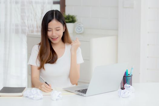Young asian woman confident working at home with laptop computer and thinking idea for planning, freelance happy girl excited and success using notebook thoughtful and writing, business concept.