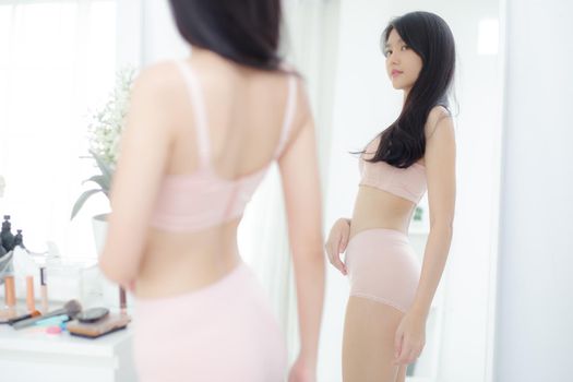 Lifestyle of beautiful young asian woman in underwear looking in mirror with belly figure slim at home, beauty body girl in lingerie shape fit with weight loss, abdomen and waist sexy perfect.