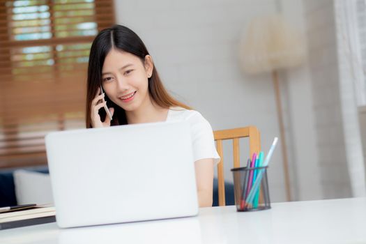 Young asian woman talking phone and work from home with laptop computer, freelance using notebook to internet online and speak on smartphone, domestic life, business and communication concept.