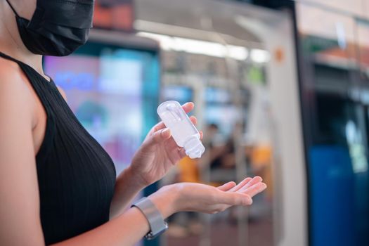 Woman wearing mask and using alcohol gel sanitizer to disinfect Covid-19 virus in metro train station.