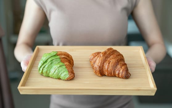 Woman serving baked crispy croissants on wooden tray.