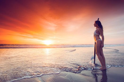 Woman holding surfboard standing disappoint in the edge of sea wave, looking forward to the sea for sufficeint wave to surf at sunset on background