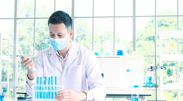 An Asian scientist or chemist drops a blue liquid chemical in a laboratory. Research concepts in healthcare, pharmacy, and medicine. Liquid analysis to separate DNA and molecules in vitro.