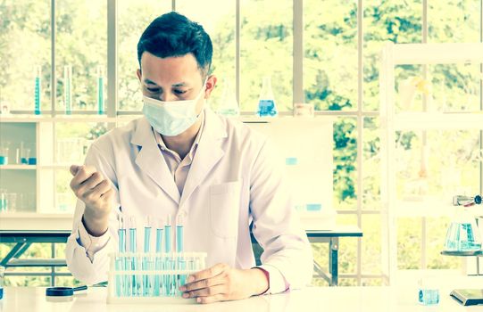 An Asian scientist or chemist drops a blue liquid chemical in a laboratory. Research concepts in healthcare, pharmacy, and medicine. Liquid analysis to separate DNA and molecules in vitro.