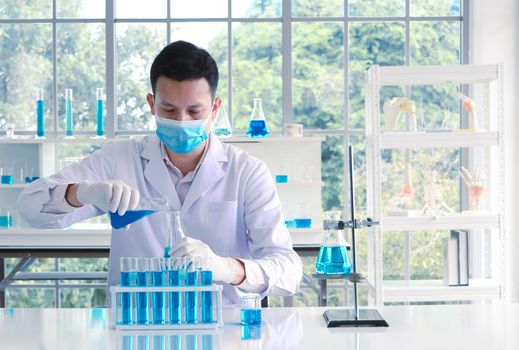 An Asian scientist or chemist drops a blue liquid chemical in a laboratory. Research concepts in healthcare, pharmacy, and medicine. Liquid analysis to separate DNA and molecules in vitro.