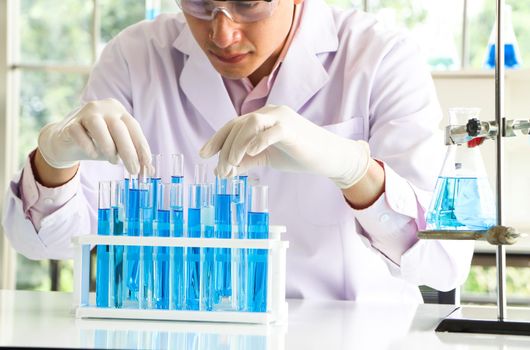 An Asian scientist or chemist drops a blue liquid chemical in a laboratory. Research concepts in healthcare, pharmacy, and medicine. Liquid analysis to separate DNA and molecules in vitro.