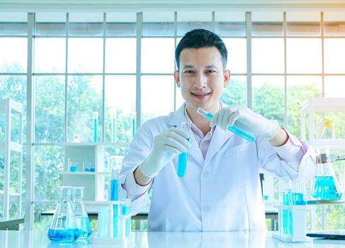 An Asian scientist or chemist drops a blue liquid chemical in a laboratory. Research concepts in healthcare, pharmacy, and medicine. Liquid analysis to separate DNA and molecules in vitro.