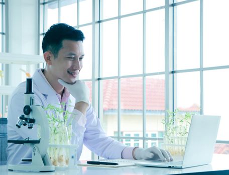 Asian researchers in white coats The concept of working in a scientific laboratory Using a laptop to find information And write down in the test results book Or making a report in a science laboratory