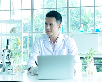 Asian researchers in white coats The concept of working in a scientific laboratory Using a laptop to find information And write down in the test results book Or making a report in a science laboratory