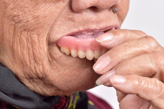senior woman putting false tooth into her mouth