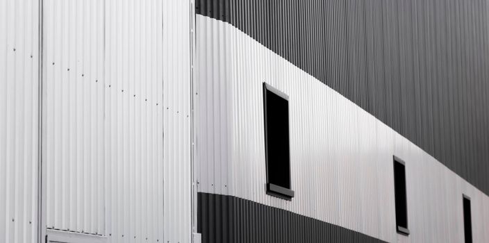 Black and white corrugated iron sheet used as a facade of a warehouse or factory with a windows. Texture of a seamless corrugated zinc sheet metal aluminum facade. Architecture. Metal texture